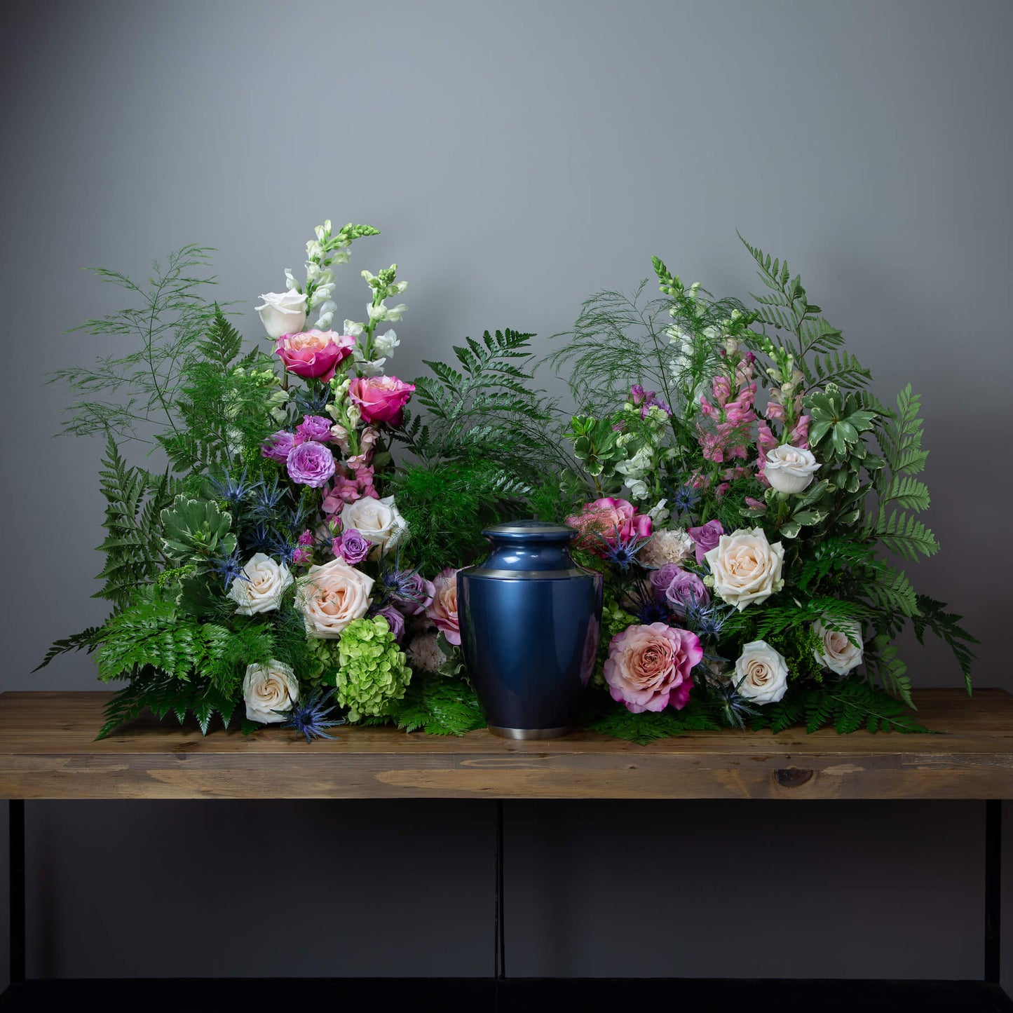 Floral arrangement with a blue urn on a wooden table against a gray background