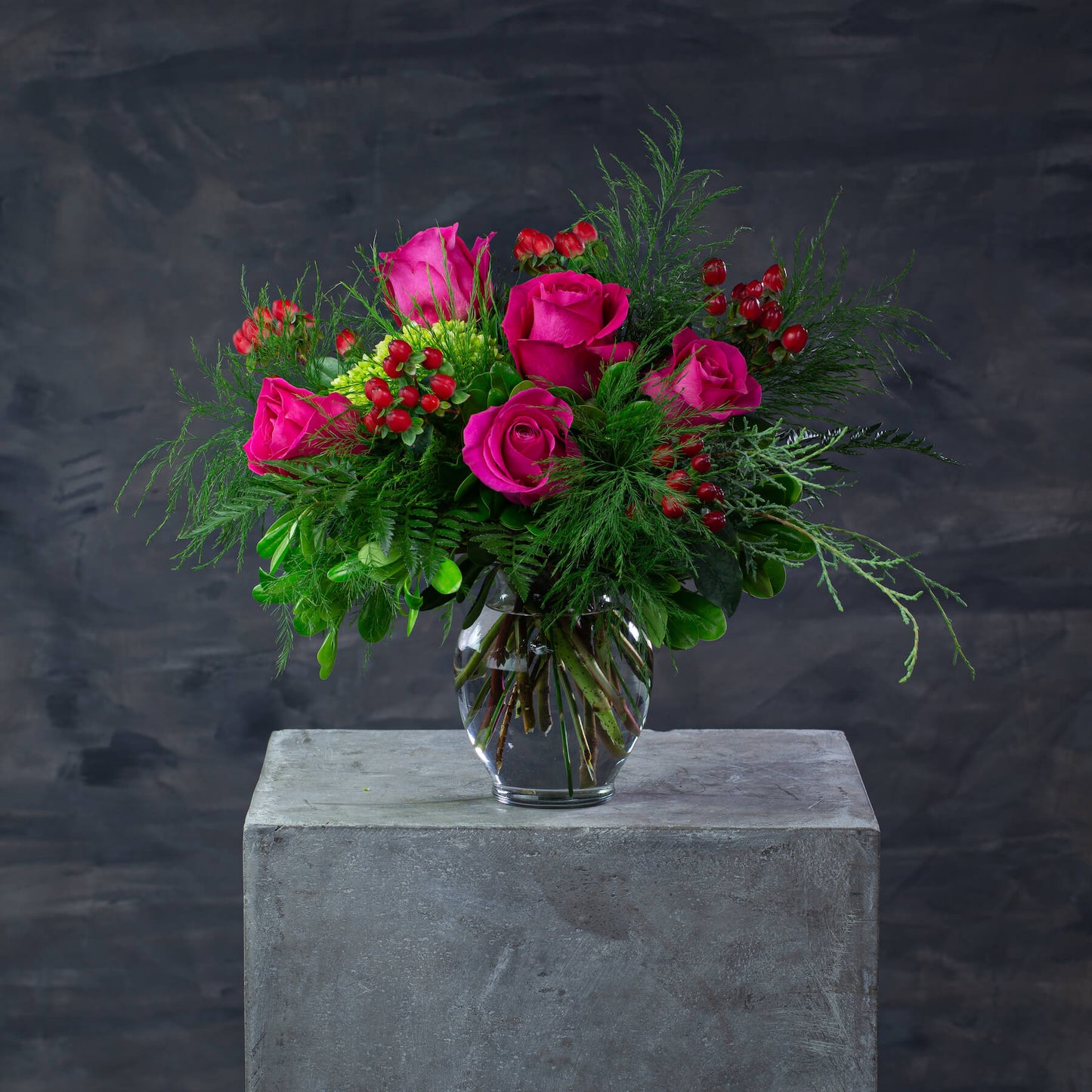 Bouquet of pink roses and greenery in a clear vase on a dark background