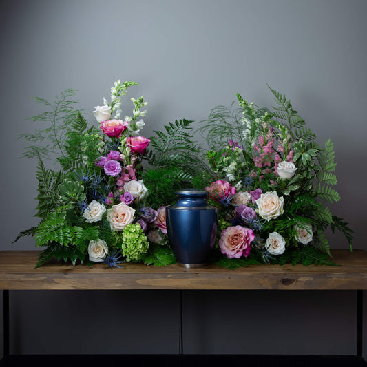 Floral arrangement with a blue urn on a wooden table against a gray background